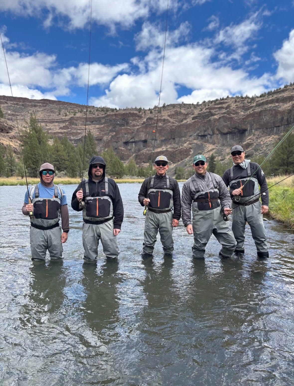 Depicts a group of people standing in a river during a fishing trip